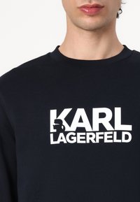 Crna pamučna dukserica s istaknutim bijelim printom logotipa "KARL LAGERFELD" i dizajnom siluete. Okrugli izrez i mekana tekstura.