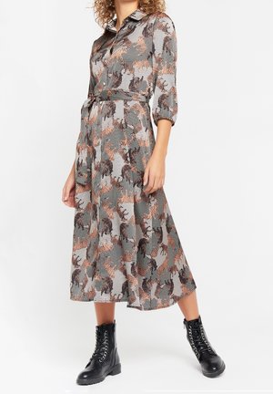 Kvinde iført midilængde kjole med knapper og krave med tigerprint, kombineret med sorte snørestøvler.