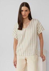 V-hals, kort mouwen top in lichtbeige met horizontale en verticale strepen. Gemaakt van een gestructureerde stof; gecombineerd met lichtgekleurde broeken.