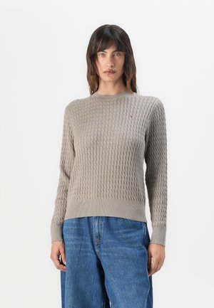 Beige knitted sweater with a textured diamond pattern, round neckline, and ribbed cuffs and hem. Small logo accent on the chest.