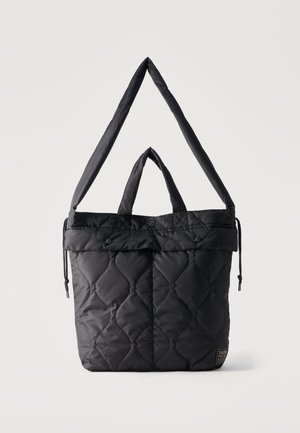 Borsa tote nera trapuntata con tasche con patta e bottone, manici corti e tracolla lunga regolabile, mostrata su uno sfondo chiaro e uniforme.