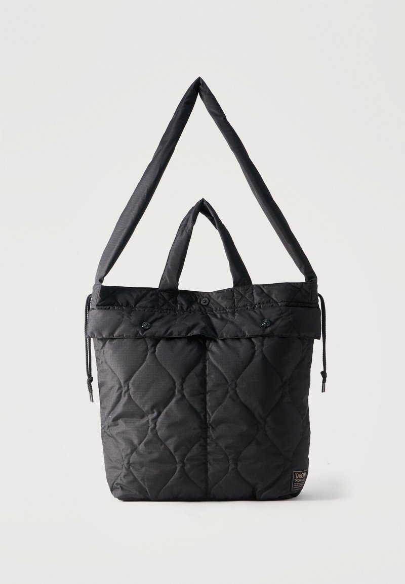 Μαύρη καπιτονέ τσάντα ώμου με τσέπες με κουμπιά στο καπάκι, κοντά χερούλια και μακρύ ρυθμιζόμενο λουρί ώμου, που προβάλλεται σε απλό φωτεινό φόντο.