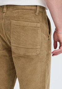 Corduroy pants in a light brown color, featuring vertical ribbing, a back pocket, and a close-fitting design.