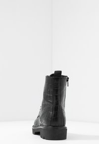Botte de cheville noire avec une texture embossée crocodile, dotée d'une fermeture éclair sur le côté, d'une languette en boucle et d'une semelle épaisse. Design simple, finition mate.