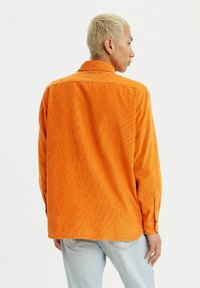 Camicia in corduroy arancione con colletto, maniche lunghe e polsini con bottoni; presenta una sottile texture a righe verticali. Adatta per un look casual.