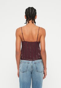 Burgundska majica na bretele z tankimi trakovi, s vertikalnimi belimi šivi, prilegajoča zasnova in gladka tekstura. Ujemajoči se z svetlo modrimi kavbojkami.
