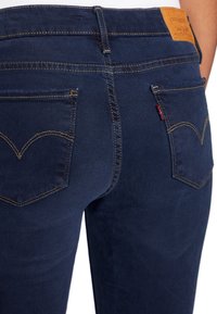 Vaqueros de mezclilla de un azul oscuro con un diseño clásico de cinco bolsillos, costuras doradas y un parche de cuero con la marca en la cintura.