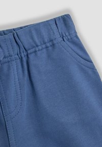 Modré tepláky s elastickým pasem, bočními kapsami a žebrovanou strukturou. Materiál vypadá měkký a flexibilní s viditelnými detaily šití.
