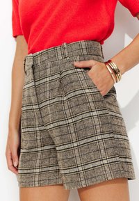 Shorts à carreaux bruns avec des lignes noires et crème, présentant une coupe ajustée, une taille haute, des poches latérales et un tissu texturé.