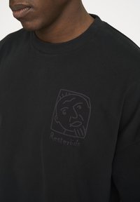 Sort bomulds t-shirt med et lilla grafik af et ansigt og teksten "Resteröds" under designet. Klassisk rund hals og afslappet pasform.