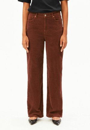 Vrouw draagt bruine corduroy wijde broek met hoge taille en voorzakken, gecombineerd met zwarte puntige schoenen en een zwart topje.