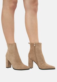 Botas de tobillo de ante beige con puntera afilada y cremallera lateral, con un tacón grueso y un acabado suave y texturizado.