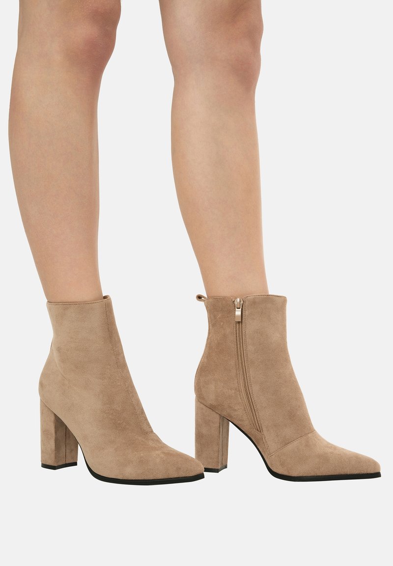 Botas de tobillo de ante beige con puntera afilada y cremallera lateral, con un tacón grueso y un acabado suave y texturizado.