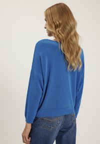Niebieski, oversize sweter o miękkiej fakturze, z prążkowanymi mankietami i okrągłym dekoltem. Posiada delikatne detale z splotu otwartego wzdłuż szwów.