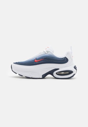 White and navy sneaker features a wavy design, smooth synthetic material, visible air unit in the heel, and red accent on the side.