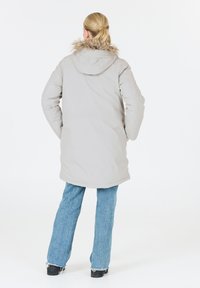 Helle graue Parkajacke mit einer gefütterten Kapuze, langen Ärmeln und geradem Schnitt, kombiniert mit blauen Schlagjeans und schwarzem Schuhwerk.