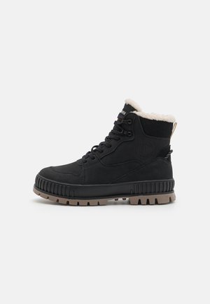 Botas de tornozelo em camurça preta com um colarinho de pelúcia sintética, ilhós de metal e uma sola de borracha castanha robusta com sulcos pronunciados e marcação.