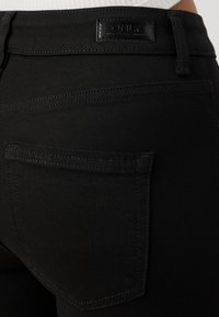Jeans de mezclilla negros con una vista en primer plano de la parte trasera y los bolsillos. La tela tiene una textura suave y un diseño minimalista, con una etiqueta de marca.