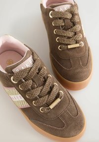 Hnědé semišové tenisky s texturovanými tkaničkami, zlatými detaily a růžovou vnitřní podšívkou. Na bocích mají pruhovaný akcent v zlaté a růžové barvě.