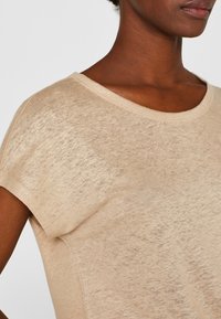 Maglietta beige a maniche corte realizzata in un tessuto leggero e leggermente texture. Presenta un colletto ampio e cuciture minime per una vestibilità rilassata.