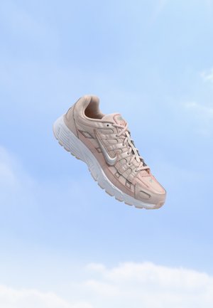 Világos rózsaszín Nike futócipő, fehér talppal, egy tiszta kék ég háttér előtt lebeg.