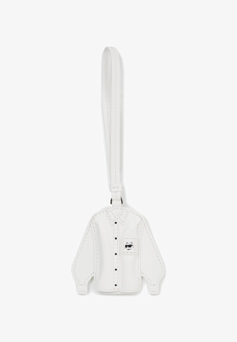 Biały skórzany brelok w kształcie koszuli z długim rękawem, z czarnymi guzikami i kieszonką zdobioną rysunkiem kota w stylu kreskówkowym. Gładka tekstura.