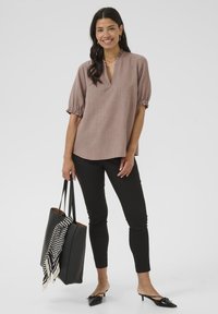 Blusa corta a maniche corte di colore rosa chiaro con scollo a V e polsini arricciati. Abbinata a pantaloni neri aderenti e una borsa a spalla nera con una sciarpa a righe.