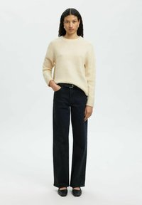 Hele beežist pehmet kootud kampsunit ümmarguse kaelusega, mis on kombineeritud kõrge vöökohaga tumesiniste laiade jalgadega teksapükstega ning mustade teravate varbava litega kingadega.