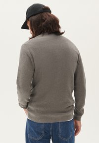 Szary dzianinowy sweter z długimi rękawami, żeberkowaną teksturą i zaokrąglonym dekoltem, noszony pod czarną czapką, w zestawieniu z niebieskimi dżinsami.