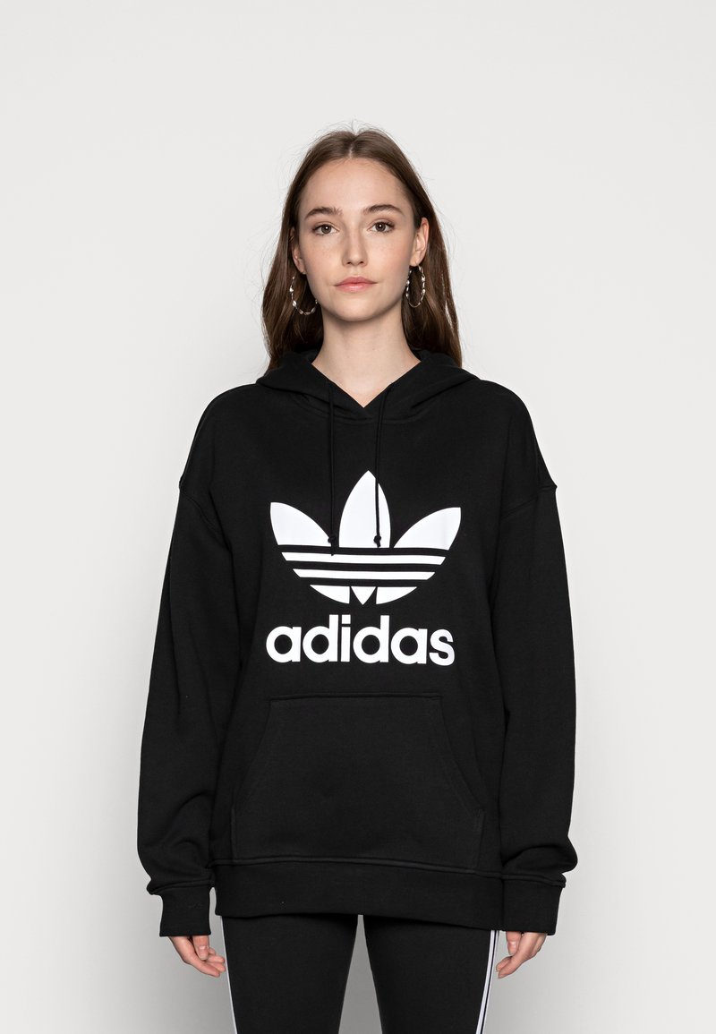 Juodas kapotas, pagamintas iš medvilnės, su dideliu baltu Adidas logotipu ir ikonine trijų juostelių dizainu priekyje. Įskaičiuota kengūros kišen�ė.