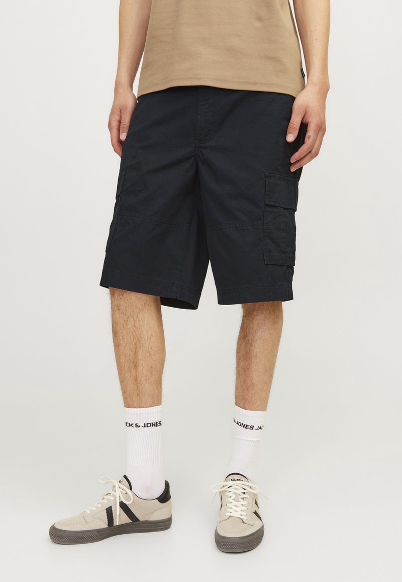 Shorts cargo navy en mélange de coton/polyester, avec plusieurs poches et une coupe régulière, associés à des baskets beiges et des chaussettes blanches.