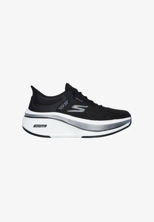 Zapatilla deportiva negra con parte superior de malla, entresuela blanca acolchada y suela exterior de goma negra texturizada. Presenta un diseño sin cordones y detalles con el logo.