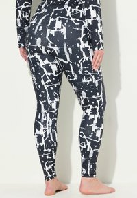 Leggings neri con design di macchie di vernice bianca astratte; tessuto liscio ed elastico; lunghezza completa; vita alta; taglio aderente.