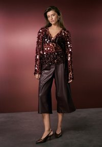 Burgundy sequin top with long sleeves, paired with brown faux leather culottes and pointed-toe heels, set against a muted background.