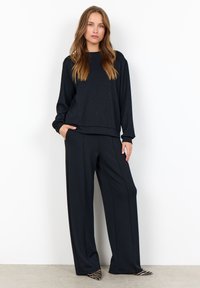 Black sweatshirt with subtle sparkles, paired with loose-fitting black trousers. Both have a smooth texture and casual design.