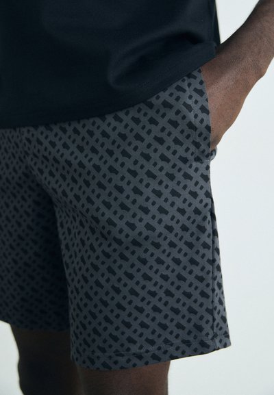Shorts noirs à motifs avec un design en grille, fabriqués en tissu léger. Les poches latérales sont visibles, avec une texture lisse.