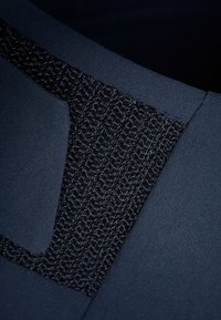 Abito blu navy con un dettaglio del collo nero testurizzato, realizzato in tessuto liscio e con un design strutturato. Il girocollo presenta un accento intrecciato.