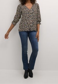 Blus med blommönster, v-ringning, trekvartsärmar och knapprad, kombinerad med figursydda blå jeans och svarta ankelboots.