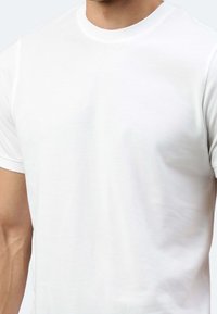 T-shirt bianco a maniche corte realizzato in tessuto di cotone. Presenta un collo rotondo e polsini a coste con una texture liscia. Design minimalista.