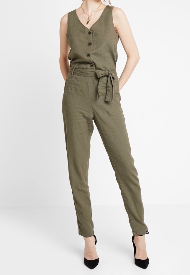 Jumpsuit de lino verde oliva con escote en V, botones frontales, detalle de cinturón en la cintura y perneras ajustadas, combinado con tacones altos negros.