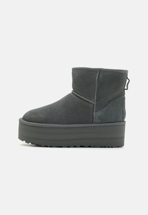 Gray suede ankle boot with a rounded toe, thick platform sole, and rear pull tab. Features contrast stitching and a ribbed sole pattern.