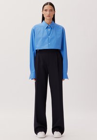 Blaues, kurzes Hemd mit Button-Down-Kragen, langen Ärmeln, kombiniert mit hochgeschnittenen schwarzen Hosen und weißen Turnschuhen. Glatte Texturen überall.