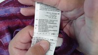 Cotton care label showing care instructions and material specifics in multiple languages, attached to a multicolored fabric with a purple pattern.