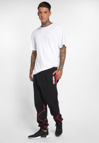 White t-shirt, black joggers with red accents and logo, and black athletic shoes. The joggers have a loose fit and cuffed ankles.