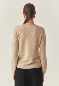 Beige wollen trui met een ruime pasvorm, lange mouwen en een brede halslijn. Zachte textuur en geribbelde zoomdetail. Gemaakt met zwarte broeken.