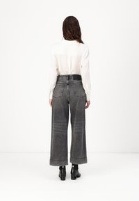 Pantalones de mezclilla anchos grises con una cintura alta, que cuentan con bolsillos traseros y una textura desgastada. Combinados con una camisa blanca de botones y botines negros.