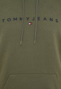 Olivovo zelená mikina s kapucňou a predným vreckom, s nápisom "TOMMYJEANS" v tmavomodrej farbe a malým detailom loga v červenej, bielej a modrej farbe. Obsahuje šnúrky.