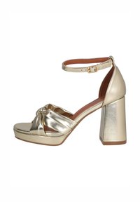 Sandalia de tacón alto metálica dorada con un tacón ancho de bloque, una correa frontal anudada y una correa en el tobillo con cierre de hebilla.