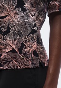Floral-patterned top in black fabric featuring light pink outlines. Includes a small gold hardware accent near the hem. Soft texture.