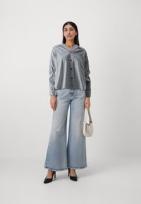 Striped button-up shirt, wide-leg blue jeans, black heels, and white handbag. Soft fabric, relaxed fit, horizontal and vertical stripes.